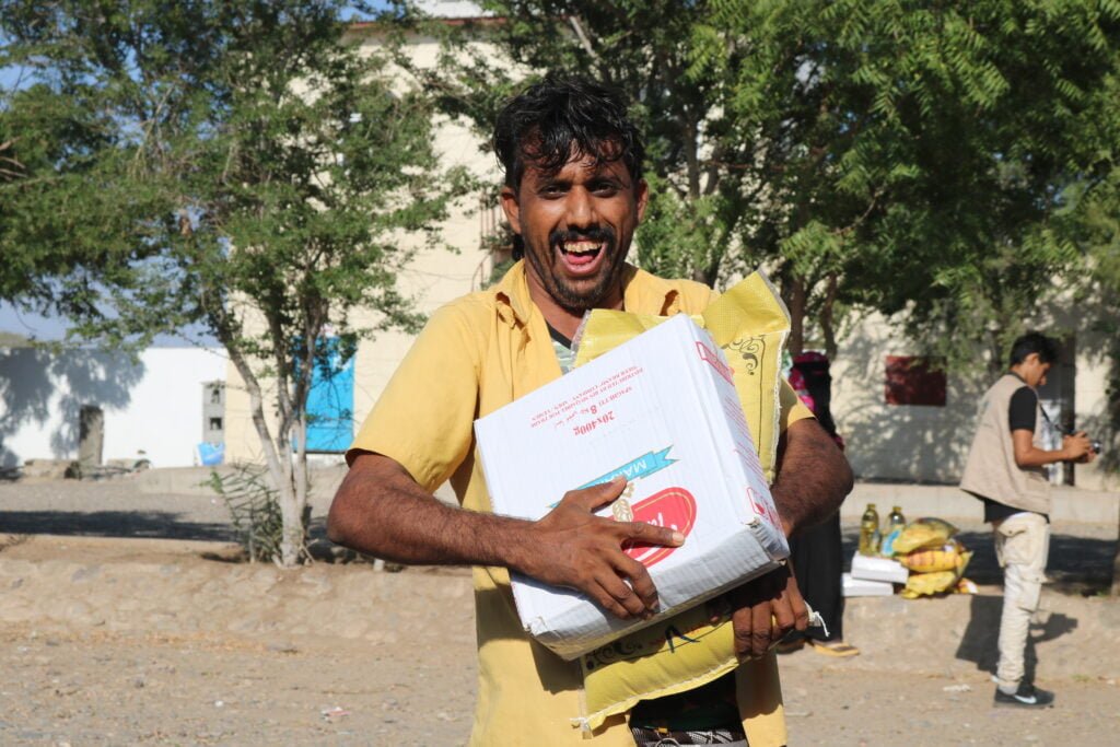 Homme au Yémen qui porte un colis alimentaire avec sourire