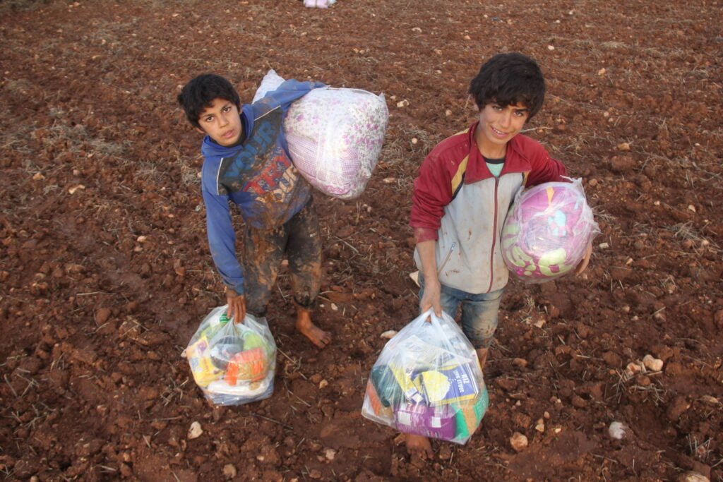 Enfants syriens pieds nus dans la boue qui portent l'aide humanitaire reçue